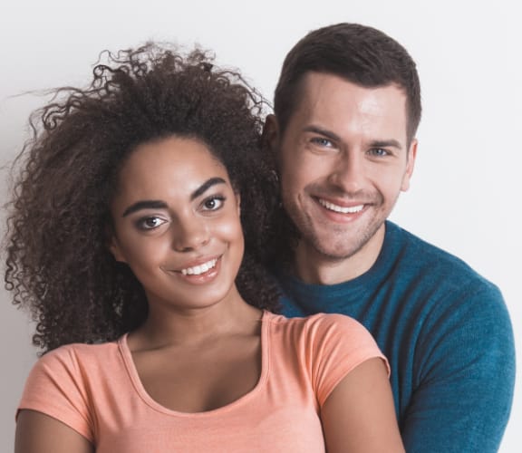 Man holding woman from behind while they both smile
